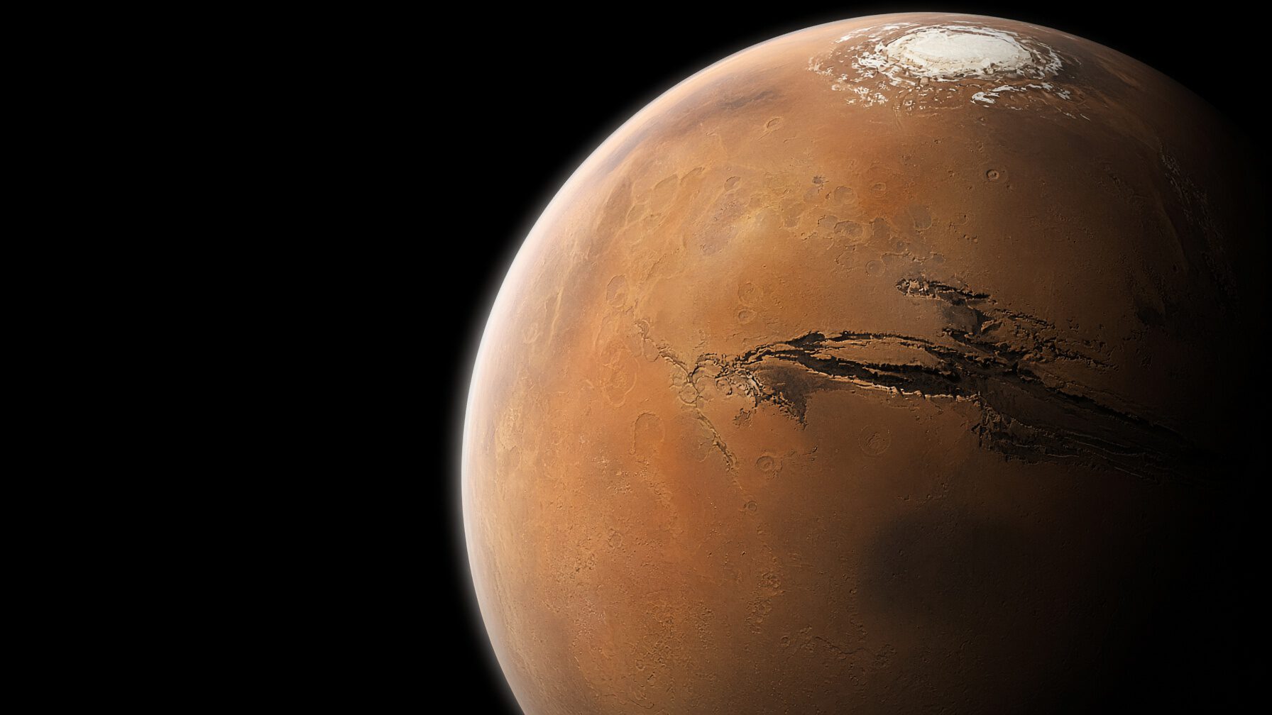 Mars photographed from high orbit near the terminator, the northern frost cap lit and the great canyon system falling into shadow.